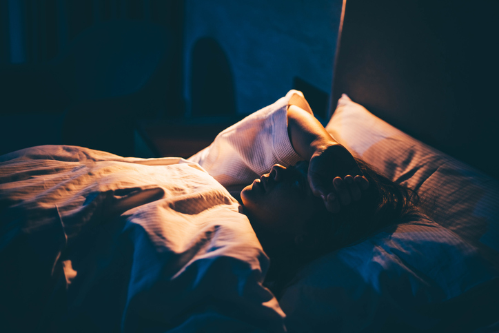 Photo shows young woman lying on bed with hand on forehead/Getty Images