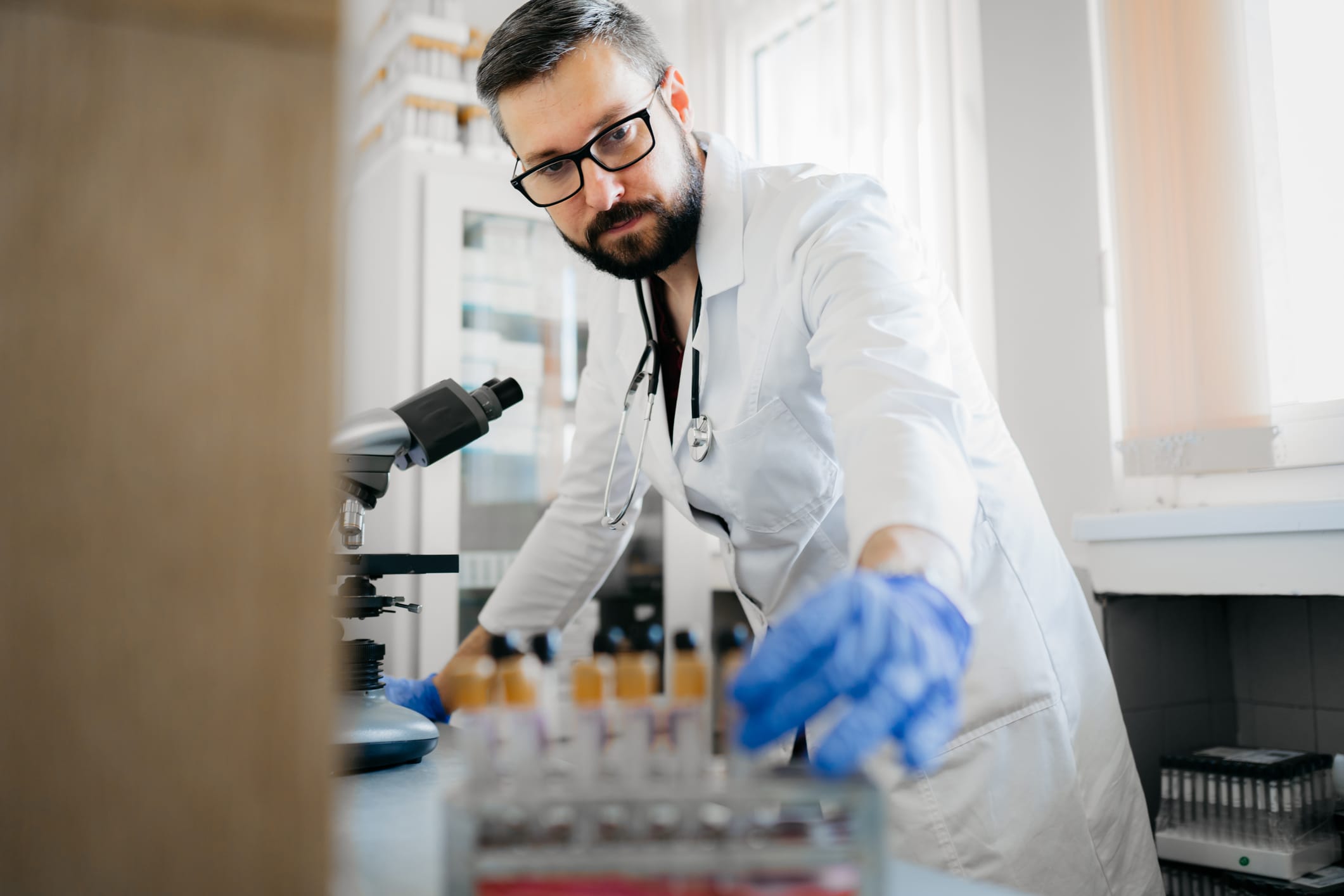 lab technician wearing a lab coat and protective gloves while using a microscope and checking blood cells