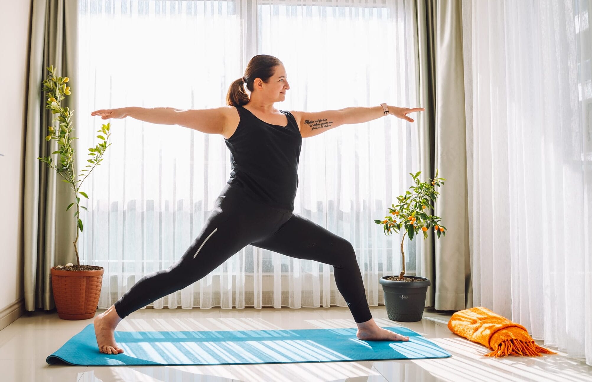 Woman plus size in black sport clothes do stretching exercises at home in living room against large window