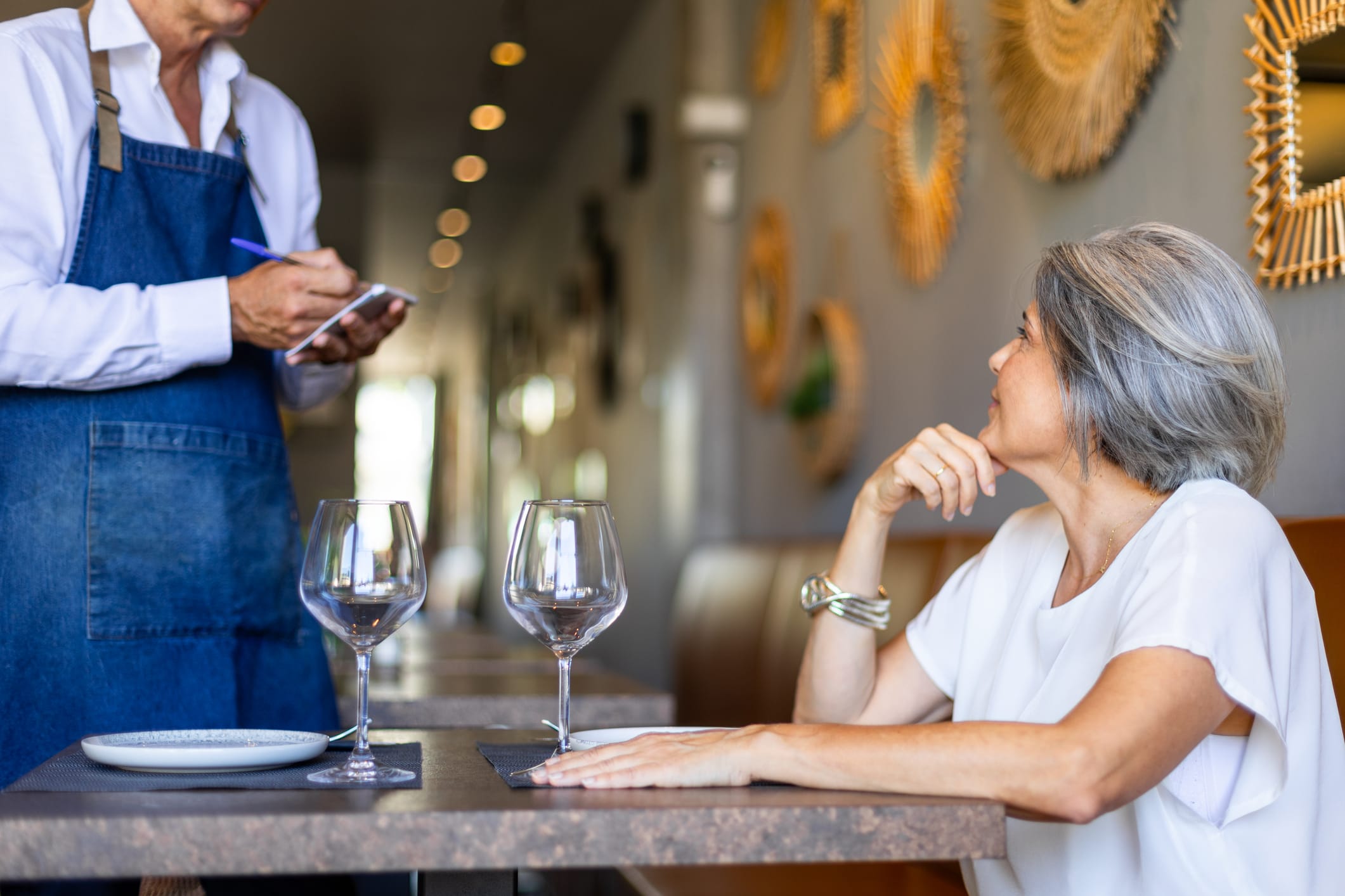 Mature woman ordering food in a restaurant with waiter taking notes, she is sitting at the table and looking away