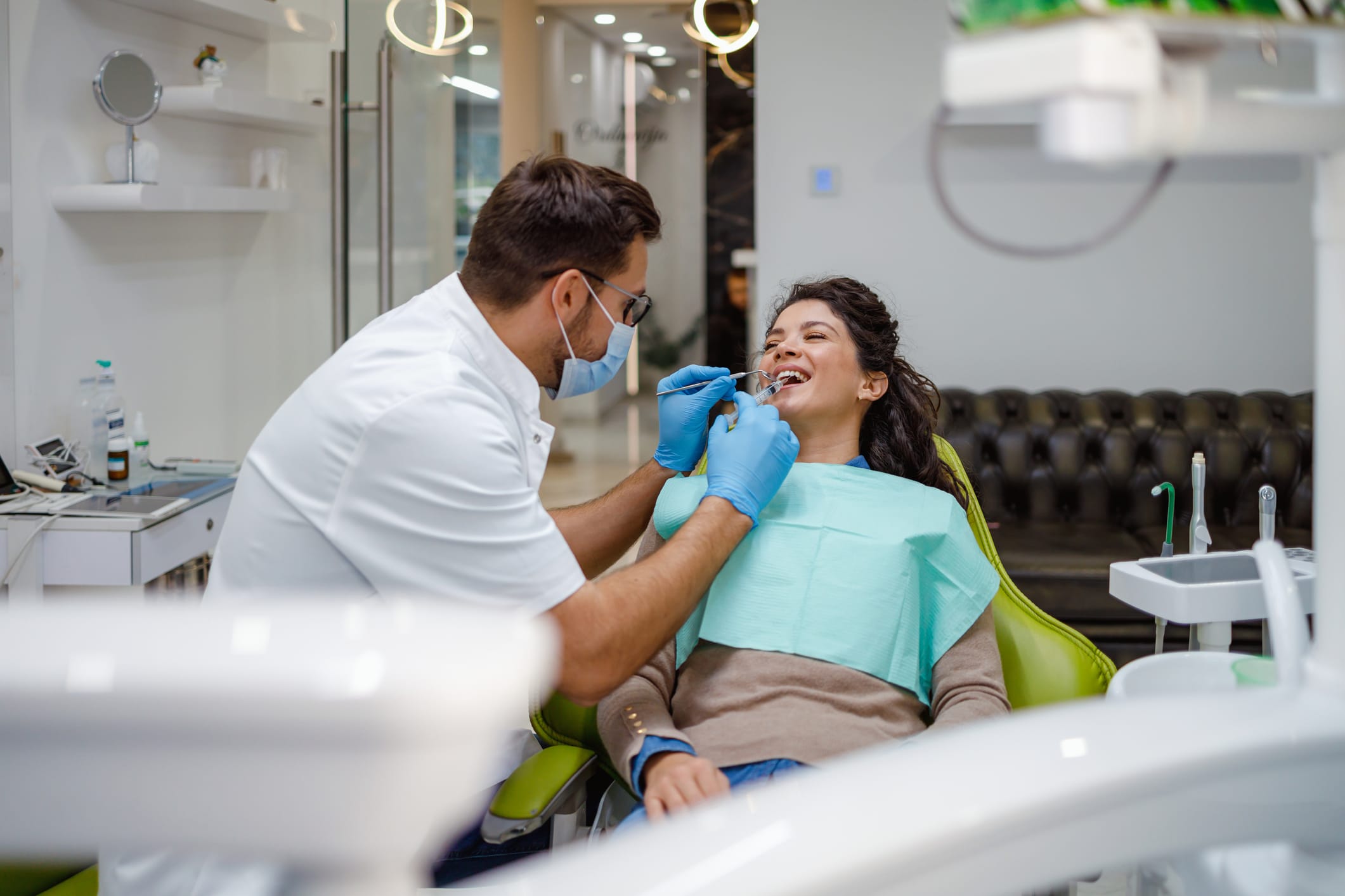 A dentist in protective gear is checking a female patient’s teeth in a modern dental office, representing healthcare