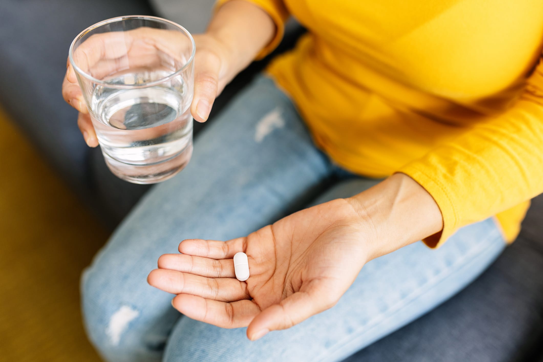 Close-up of woman holding pill in one hand and glass of water in the other.